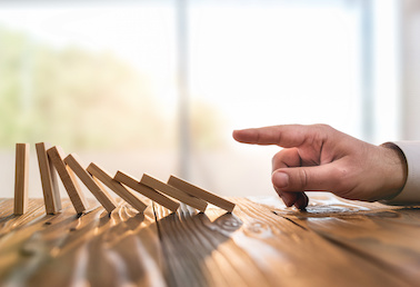 Image of man's hand pushing over dominoes