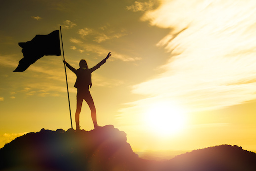 silhouettes of girl with flag of victory on the top of a mountain