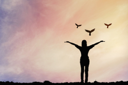 Image of woman releasing three birds into sunrise