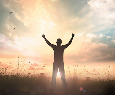 Image of a man with upraised arms facing sunrise