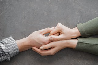 Image of woman's hands holding a young man's hand to comfort him; on grey background