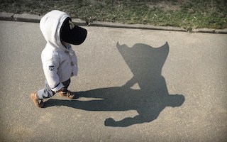 Image of a young boy whose shadow on the sidewalk is superman with a cape