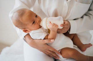 Image of newborn baby boy being held and bottle-fed by his mother