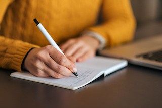 Image of person in orange sweater writing in a notebook with a pen