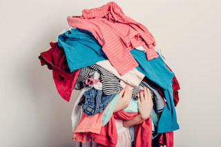 Image of girl's arms carrying a pile of clothing so big that it covers her face & body!