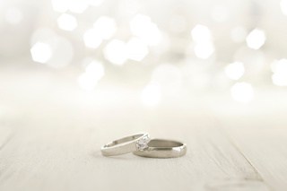Image of two wedding rings placed on wooden floor with lights in background.