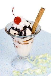 Image of a hot fudge sundae on a blue countertop with cherry & cinnamon stick