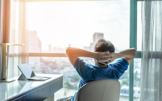 Image of a man at a modern desk looking out a high rise window at the city