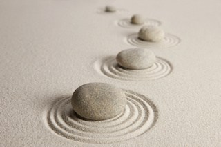 Image of stones arranged in a semi-circle on sand with concentric circles in the sand around each stone