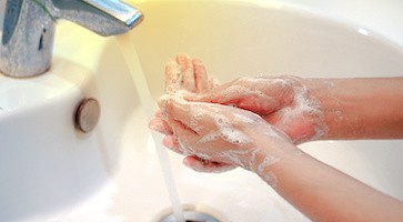 Image of white sink with hands washing with soap, the tap running
