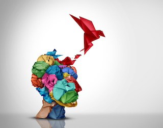 Image of bust of head made of cloth scrunchies with a red origami-style bird flying out of it against a pale sepia background